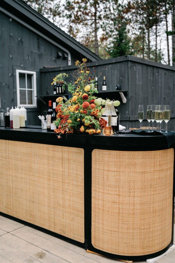 A black-framed rattan bar topped with an autumnal floral arrangement.