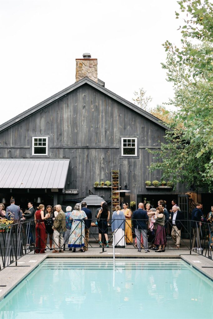 Wedding guests mingling against the A-frame exterior of a barn-like building with a gated pool.