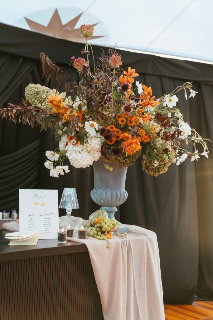 A big Dutch masters-inspired floral arrangement with green grapes at a decadently cloth-draped bar. 