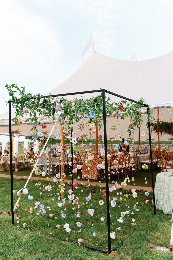 An interactive photo booth: a standing cube filled with dangling flowers and foliage