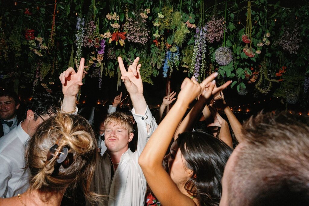 A dense floral overhang above a wedding dance floor, with several guests dancing beneath it.