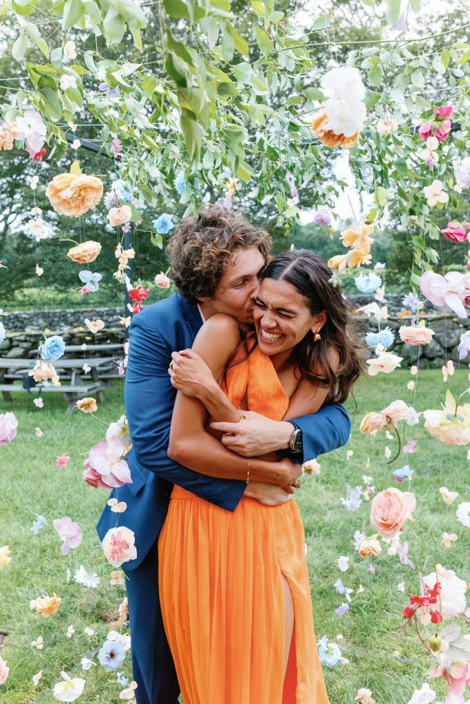 A couple embracing and smiling amidst a cascading canopy of flowers.