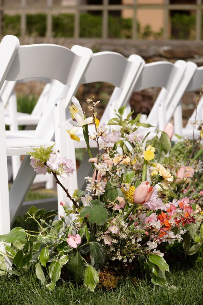 A spring flower ground arrangement beside the seats at a wedding. It contains tulips, fruit tree blooms, daffodils, and more.