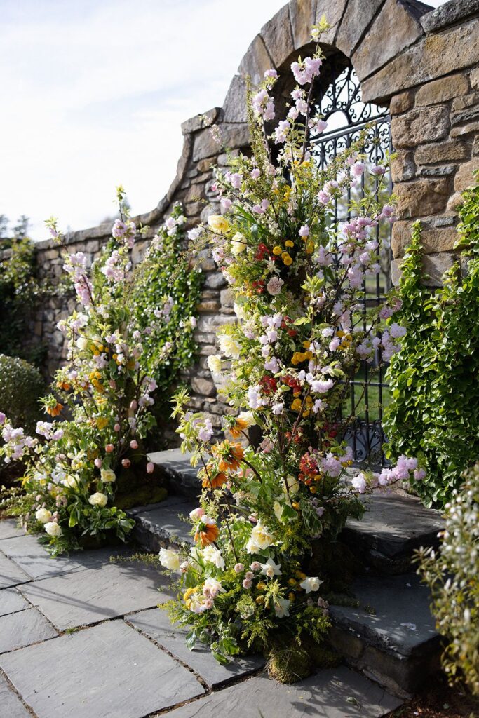 A deconstructed wedding flower arch crafted from spring blooms—including fruit blossoms, peonies, daffodils, and more.