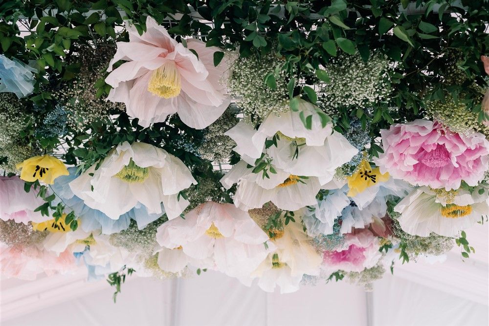 A closeup on a floral overhang with giant paper flowers at a wedding reception.