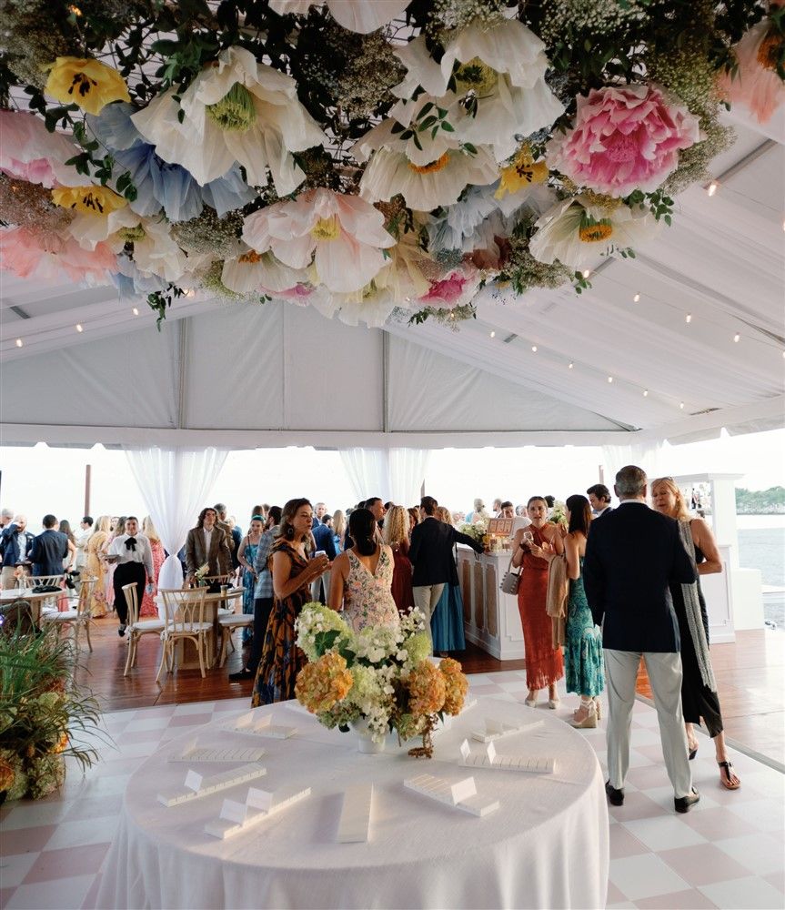 A wedding reception with a floral overhang with giant paper flowers and a dynamic hydrangea arrangement centerpiece below.