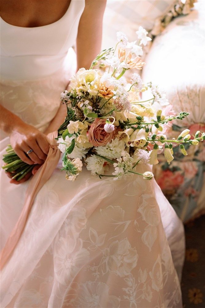 A bride with a peach-hued gown, sitting a holding a pastel bouquet in her lap.