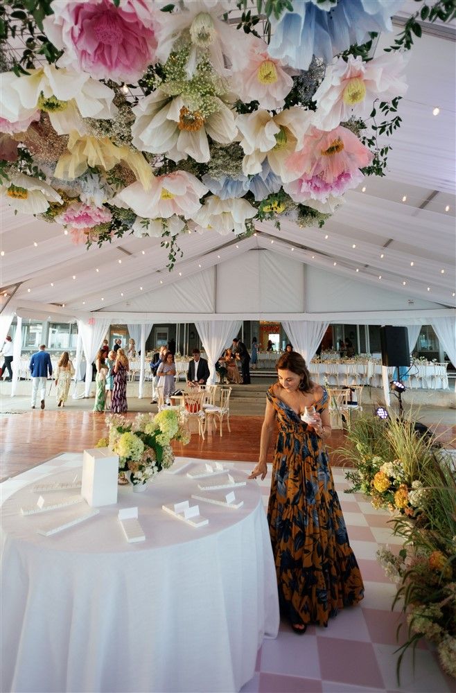 A wedding reception with a floral overhang with giant paper flowers and arrangements with long grasses below.