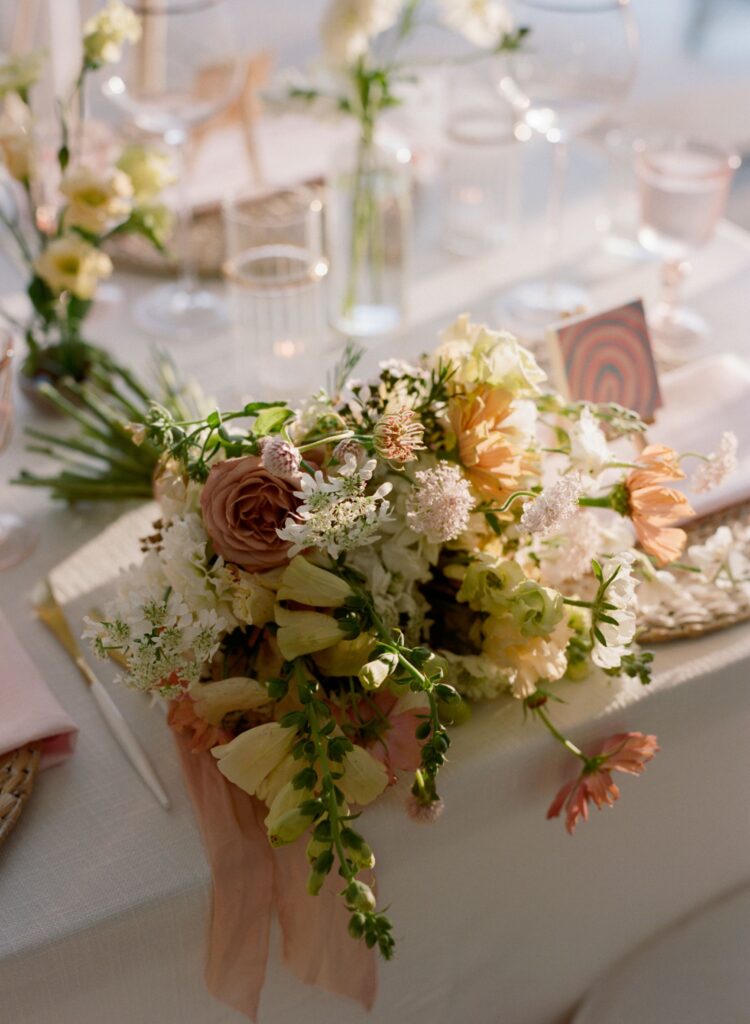 A pastel wildflower-esque bouquet sitting on a fully set wedding reception table.