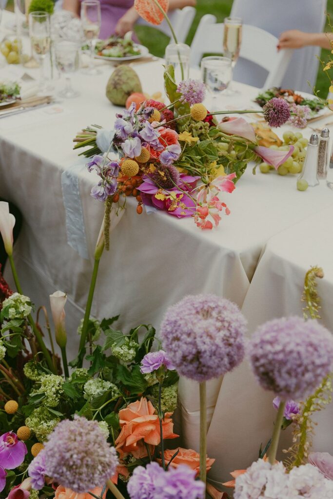 A colorful pastel sweetheart table floral arrangement and bouquet featuring fluffy purple-tipped allium.