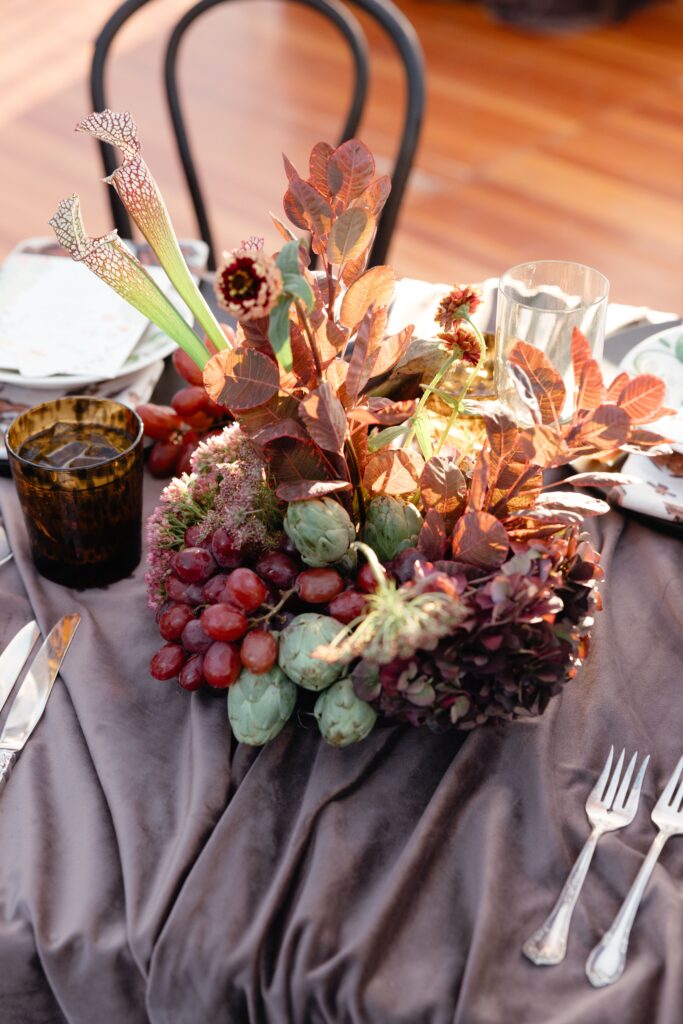 A floral arrangement of grapes, artichokes, sarracenia, and more.
